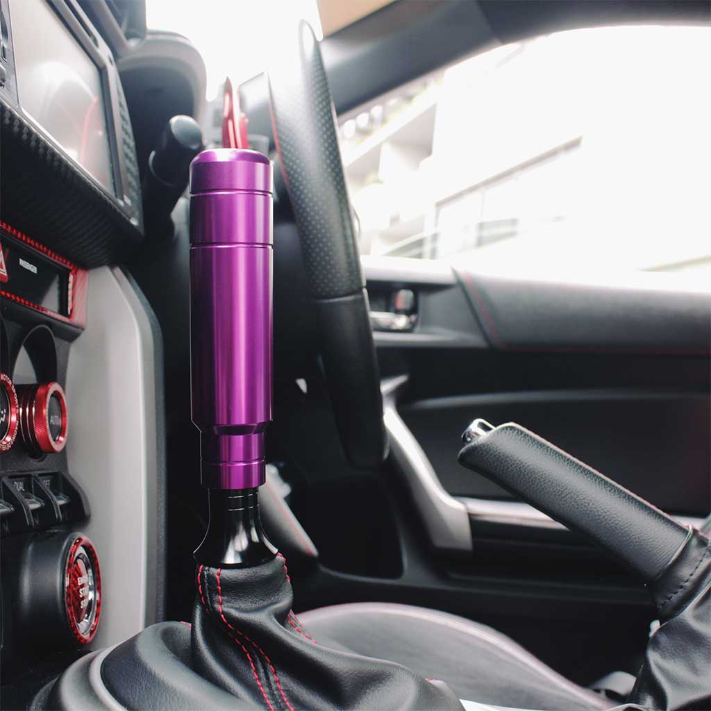 A purple aftermarket shift knob with a boot retainer underneath installed in an automatic GT86
