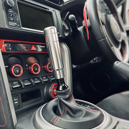 A silver aftermarket shift knob with a boot retainer underneath installed in an automatic GT86