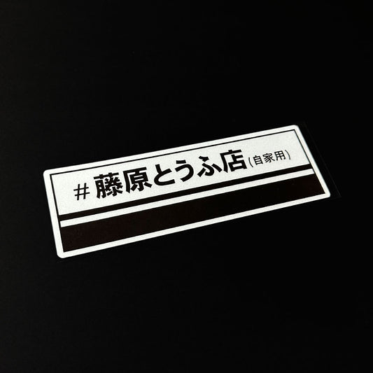 An Intial D Fujiwara tofu shop slap sticker flat laid on a black background