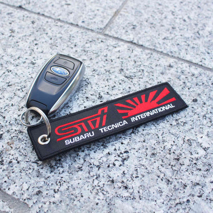 A black sti jet tag with a rising sun holding a wrx car key on a marble floor