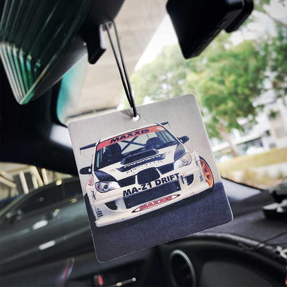 A Subaru rally car air freshener hung on a car's rearview mirror