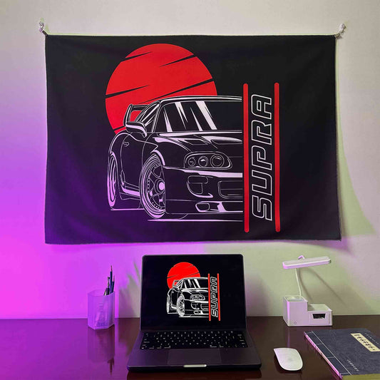 A Supra artwork hung on a wall, with a laptop showing the same photo as the wall poster underneath, lit by purple spotlight