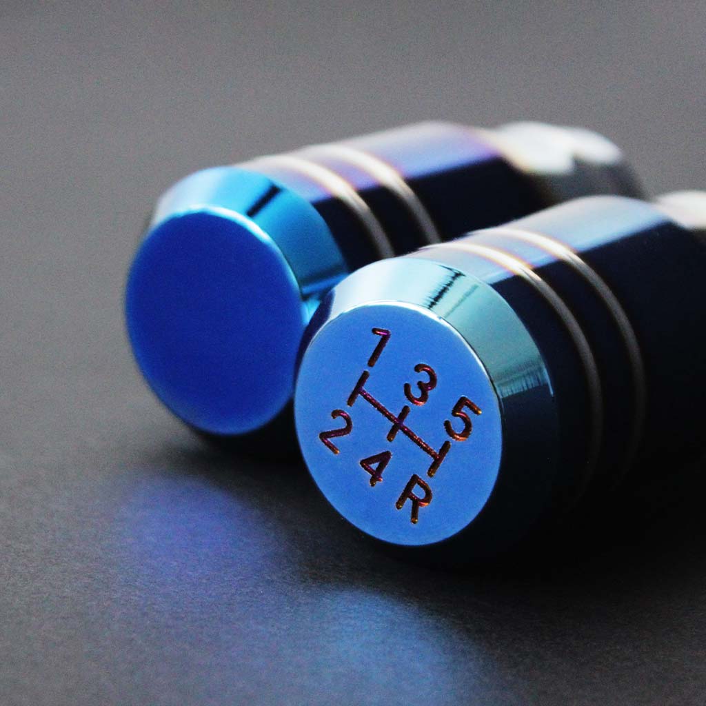 Two burnt blue shift knobs are placed closely on a dark grey background, showcasing the top section of the knobs for auto and five-speed manual cars