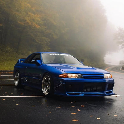 A white TOYO TIRES car vinyl decal applied on a blue GTR's front window, and the car is parked on a mountain road where it is foggy and misty