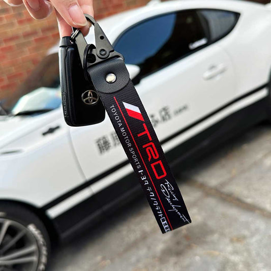 A hand holding a Toyota TRD keychain with a white 86 in the background