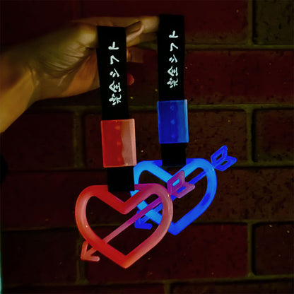 A hand holding two glow-in-the-dark tsurikawas which are in the cupid shape and their colours are red and blue